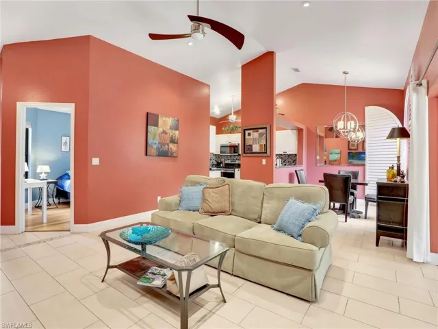 Living area with light tile patterned floors, baseboards, ceiling fan with notable chandelier, and lofted ceiling