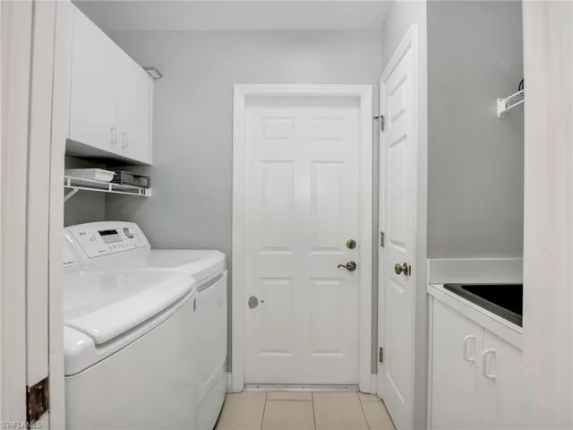 Laundry area with a sink, cabinet space, independent washer and dryer, and light tile patterned floors