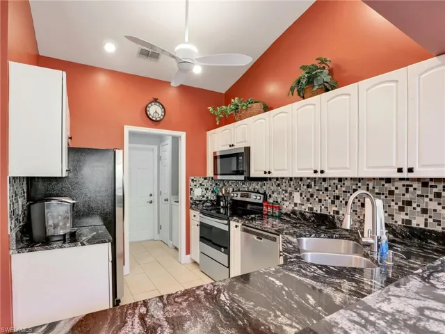 Kitchen with ceiling fan, visible vents, appliances with stainless steel finishes, a sink, and dark stone countertops