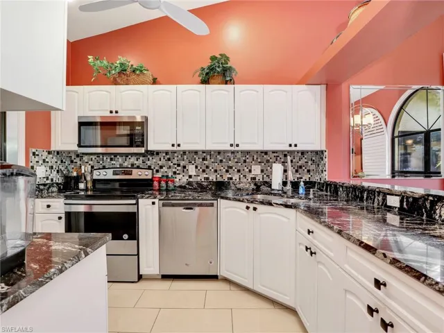 Kitchen with white cabinetry, dark stone countertops, light tile patterned flooring, and stainless steel appliances