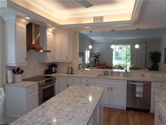 Kitchen with crown molding, stainless steel appliances, wall chimney range hood, white cabinets, and dark wood-style flooring