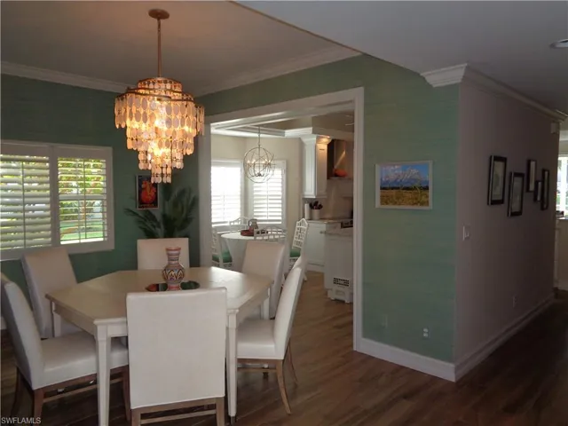 Dining area featuring ornamental molding, healthy amount of natural light, dark wood-type flooring, and a chandelier