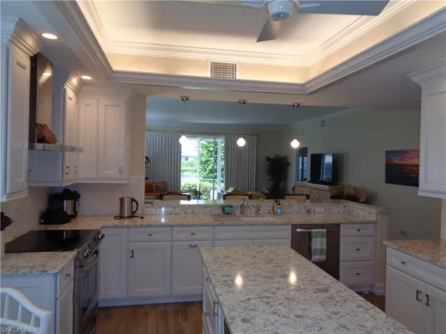 Kitchen featuring appliances with stainless steel finishes, wall chimney exhaust hood, crown molding, white cabinets, and a raised ceiling