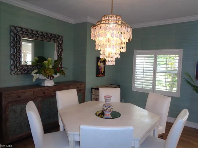 Dining area featuring a chandelier, ornamental molding, wood finished floors, and wallpapered walls