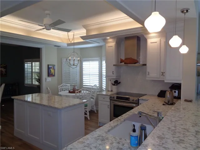 Kitchen featuring stainless steel range with electric cooktop, a ceiling fan, wall chimney range hood, ornamental molding, and white cabinets
