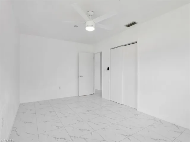 Spacious room featuring white walls, large format tile flooring, a ceiling fan with integrated lighting, and a closet with bifold doors