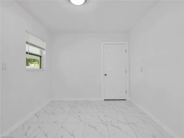 Bright interior space featuring white walls, a single window, a paneled door, and large format marble-look tile flooring