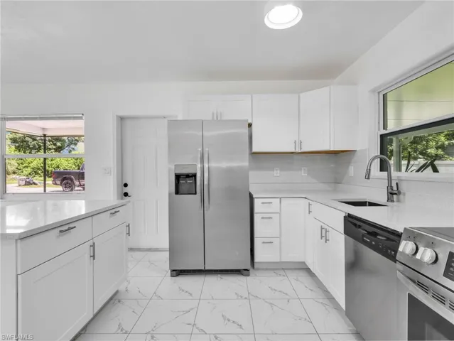 Modern kitchen featuring white shaker cabinetry, stainless steel appliances, marble-look tile flooring, light-toned countertops, and a single basin sink with a gooseneck faucet