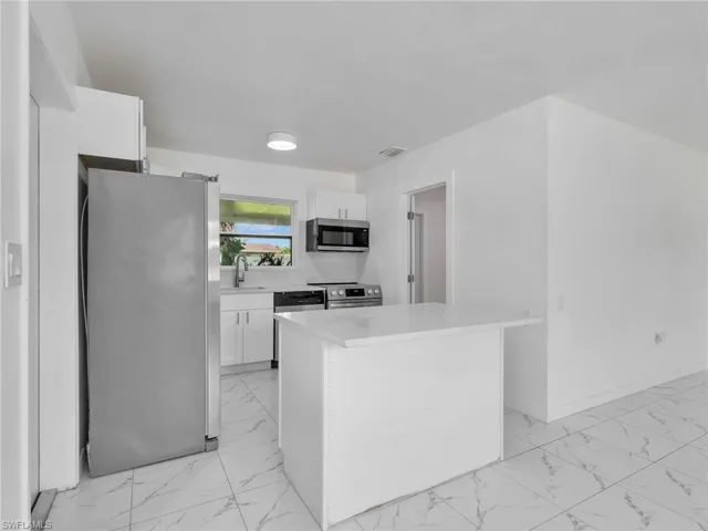 Modern kitchen featuring white cabinetry, stainless steel appliances, a white quartz countertop island, and white tile flooring