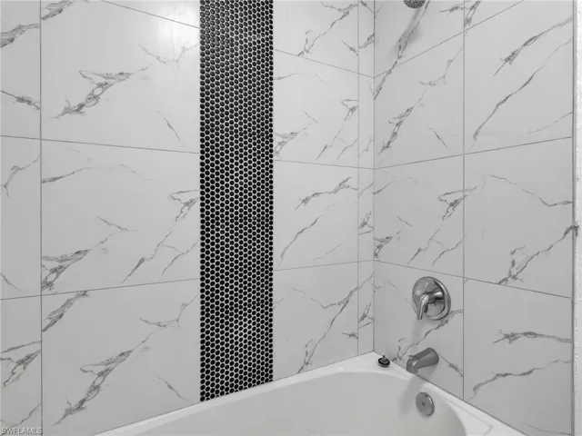 Bathtub and shower combination featuring white large-format wall tiles with grey veining, a black hexagonal mosaic accent strip, and chrome fixtures
