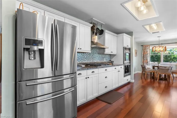 Kitchen featuring stainless steel appliances, white cabinetry, a chandelier, dark wood-type flooring, and hanging light fixtures
