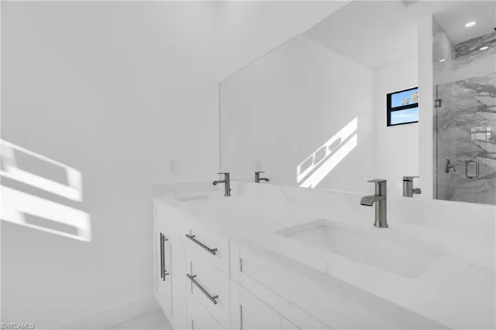 Full bathroom with a sink, a marble finish shower, baseboards, and double vanity