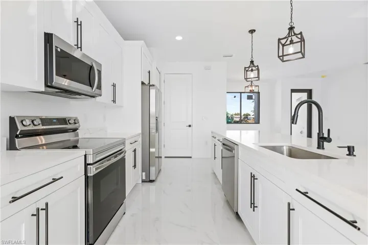 Kitchen with white cabinets, appliances with stainless steel finishes, marble finish floor, pendant lighting, and a sink