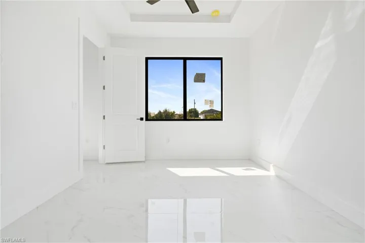Empty room featuring a ceiling fan, a tray ceiling, marble finish floor, and baseboards