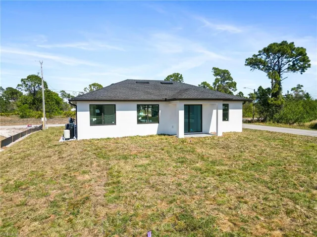 Rear view of house with roof with shingles, a yard, and stucco siding