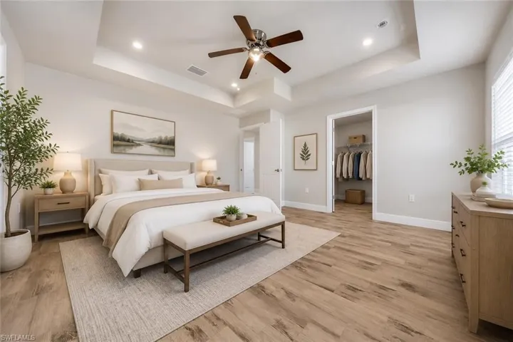 Spacious bedroom featuring a tray ceiling with recessed lighting and a ceiling fan, wood-finish flooring, and light-filtering window blinds