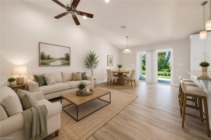 Vaulted ceiling with a ceiling fan, light wood-finish flooring, sliding glass doors to the exterior, kitchen island with seating, and pendant lighting
