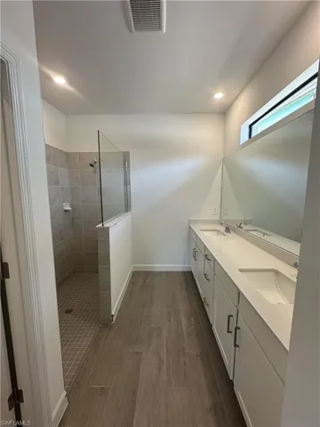 Bathroom featuring tiled shower, dual vanity, and wood-type flooring