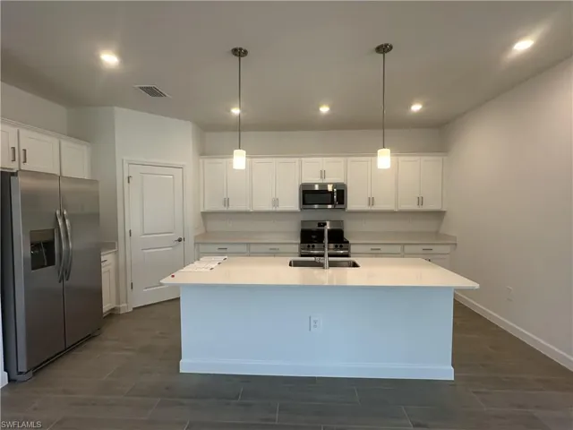 Kitchen with appliances with stainless steel finishes, hanging light fixtures, white cabinets, and a kitchen island with sink