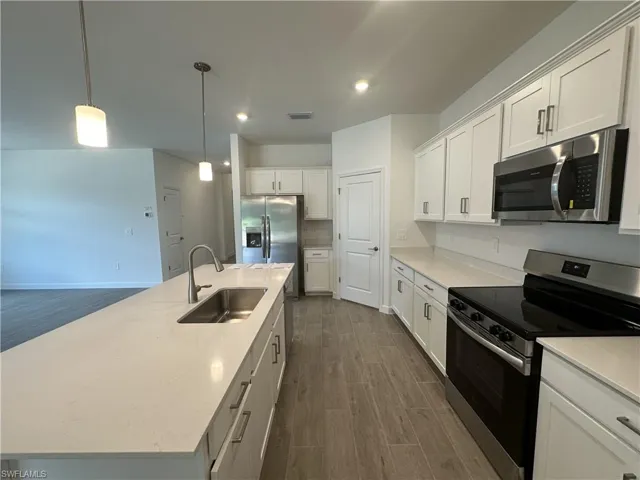 Kitchen featuring appliances with stainless steel finishes, sink, decorative light fixtures, a kitchen island with sink, and dark hardwood / wood-style flooring