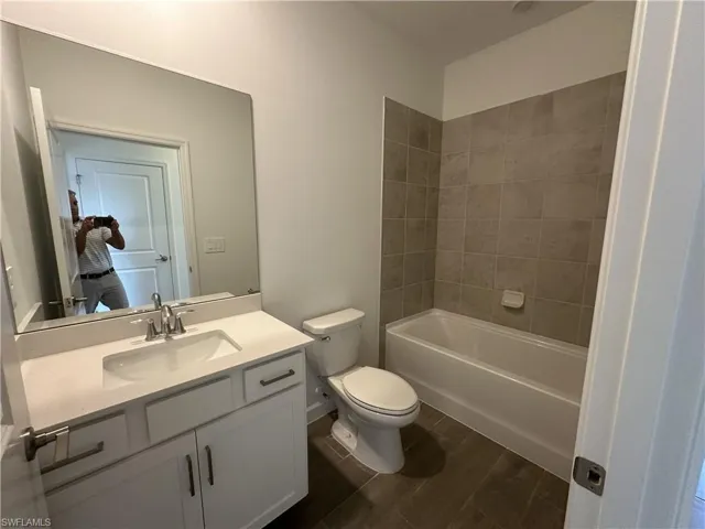 Full bathroom with hardwood / wood-style floors, vanity, tiled shower / bath combo, and toilet