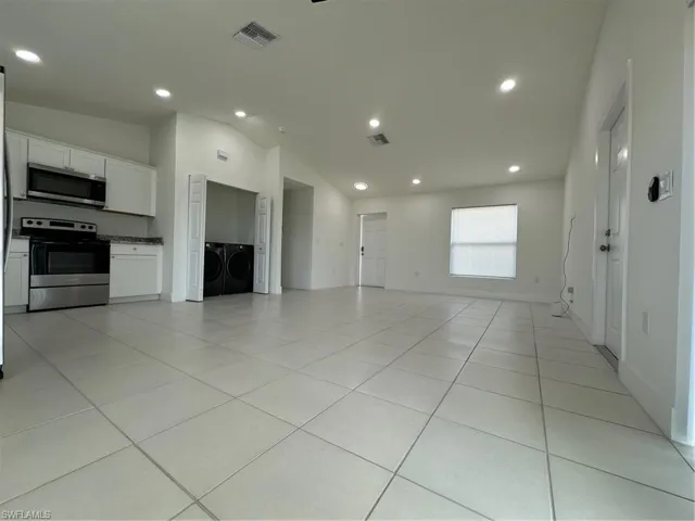 Unfurnished living room with independent washer and dryer, vaulted ceiling, light tile patterned floors, recessed lighting, and baseboards