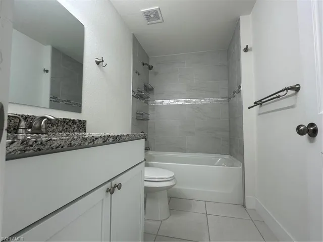 Full bath with toilet, tile patterned floors, vanity, and washtub / shower combination