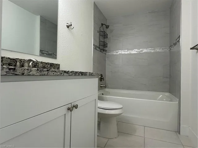 Bathroom with toilet, washtub / shower combination, vanity, and tile patterned floors