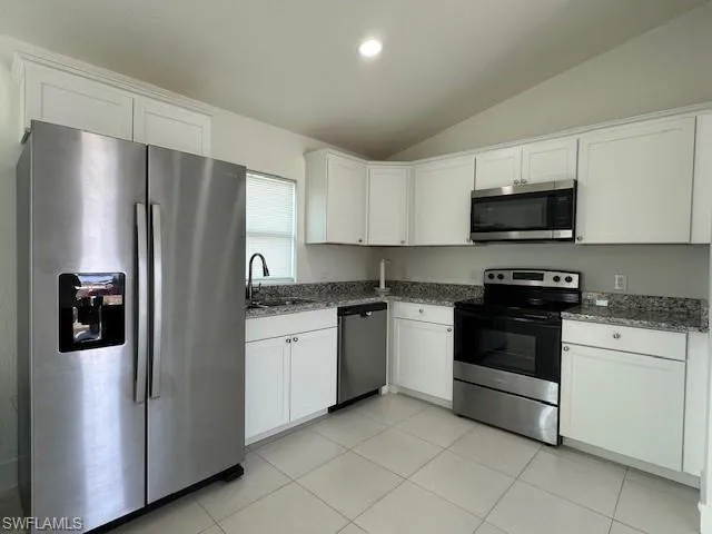 Kitchen featuring appliances with stainless steel finishes, lofted ceiling, a sink, dark stone countertops, and white cabinets