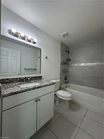 Full bath with a textured ceiling, shower / bath combination, toilet, vanity, and tile patterned flooring