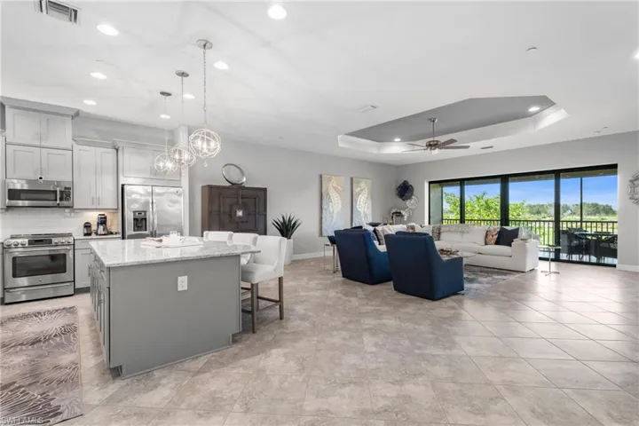 Living room with ceiling fan, a raised ceiling, baseboards, recessed lighting, and a chandelier