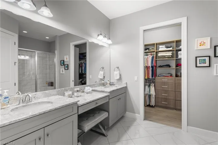 Full bathroom featuring double vanity, a walk in closet, a stall shower, baseboards, and marble look tile flooring