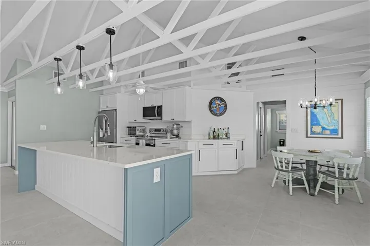 Kitchen featuring appliances with stainless steel finishes, sink, a large island with sink, decorative light fixtures, and white cabinets