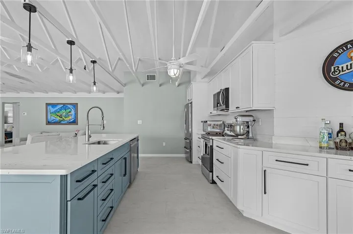 Kitchen featuring white cabinetry, sink, stainless steel appliances, light stone counters, and decorative light fixtures