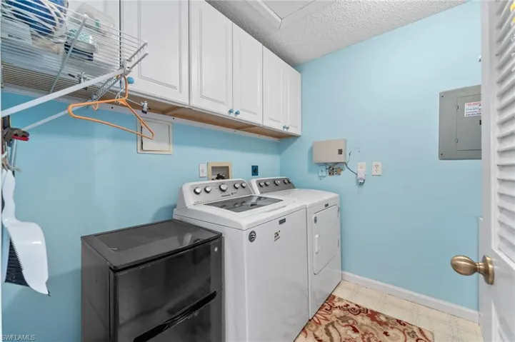 Washroom featuring electric panel, a textured ceiling, washing machine and dryer, baseboards, and cabinet space
