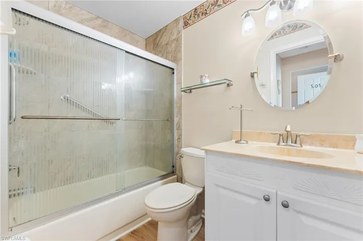 Full bathroom with enclosed tub / shower combo, toilet, vanity, and wood finished floors