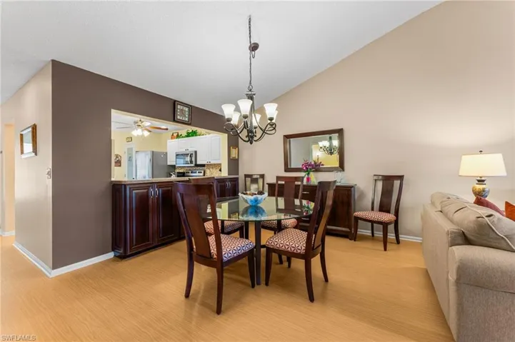 Dining space with high vaulted ceiling, light wood finished floors, baseboards, and ceiling fan with notable chandelier