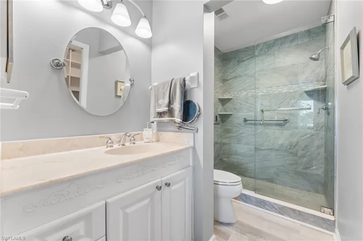 Full bath with a shower stall, wood finished floors, vanity, toilet, and visible vents