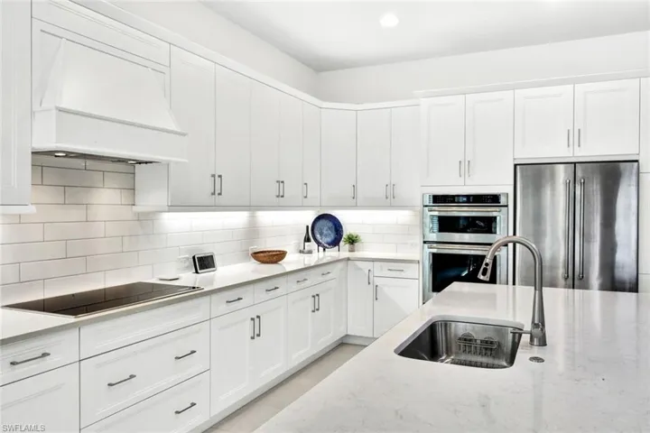 Kitchen with stainless steel appliances, white cabinets, light stone countertops, recessed lighting, and backsplash