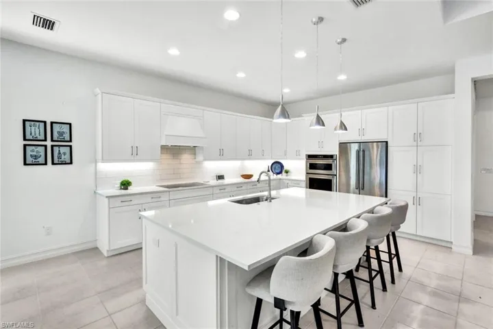 Kitchen featuring white cabinetry, a kitchen bar, decorative light fixtures, an island with sink, and stainless steel appliances