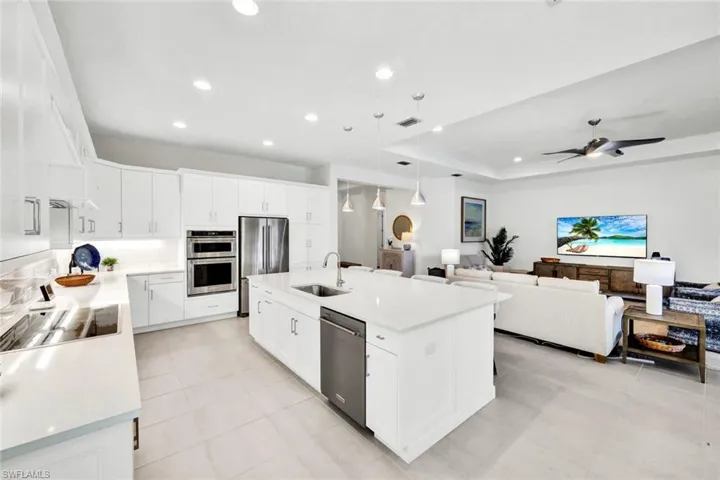 Kitchen with decorative light fixtures, white cabinetry, stainless steel appliances, a kitchen island with sink, and a raised ceiling