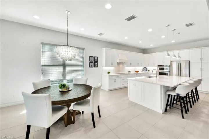 Kitchen with a center island with sink, white cabinets, a kitchen breakfast bar, stainless steel appliances, and hanging lights