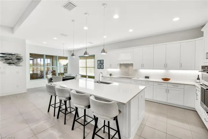 Kitchen featuring white cabinets, an island with sink, hanging light fixtures, a kitchen bar, and tasteful backsplash