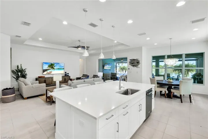 Kitchen featuring a tray ceiling, white cabinets, open floor plan, an island with sink, and light stone counters