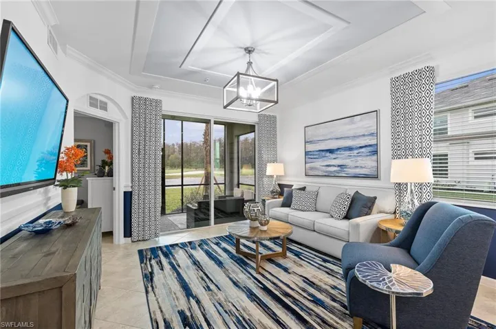 Living room with a raised ceiling, light tile patterned floors, a chandelier, and ornamental molding