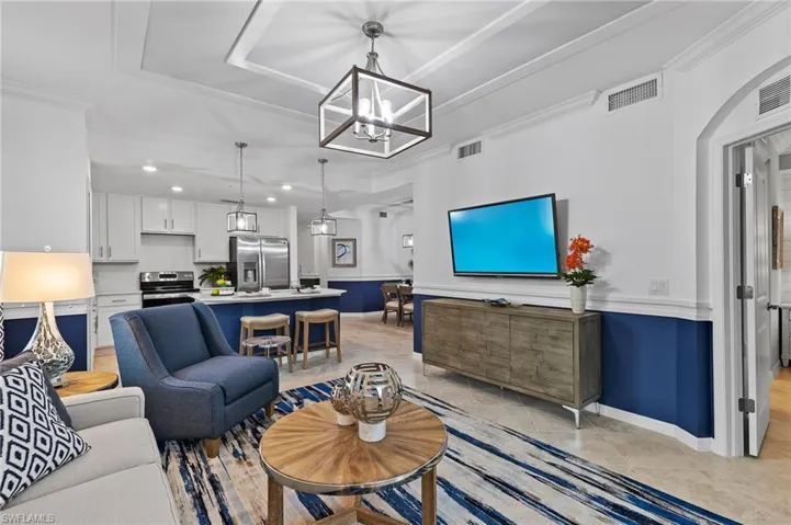 Living area with a raised ceiling, a chandelier, light tile patterned flooring, ornamental molding, and recessed lighting