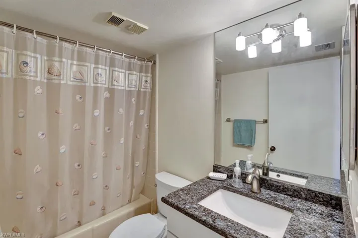 Full bathroom featuring shower / tub combo with curtain, vanity, a textured ceiling, and toilet