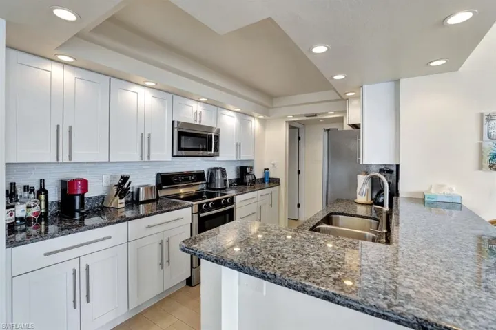 Kitchen with white cabinets, appliances with stainless steel finishes, dark stone countertops, and sink