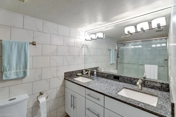 Bathroom featuring a textured ceiling, toilet, a shower with door, vanity, and tile walls