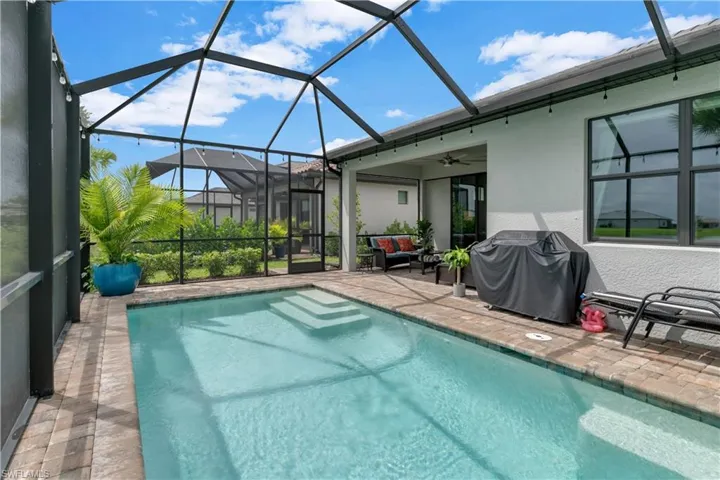 View of pool with grilling area, a lanai, a patio, an outdoor living space, and ceiling fan